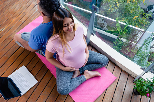 top view man and pregnant woman, young caucasian couple, lying on back, sitting on mat with laptop, in online yoga class