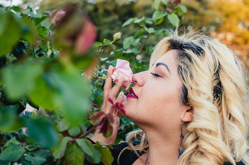 beautiful blonde caucasian young woman with eyes closed outdoors smelling a flower in the garden, copy space.