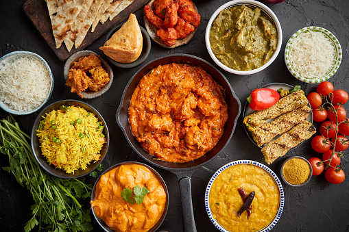Assortment of various kinds of Indian cousine on dark rusty table. Chicken Tikka Masala, Butter, Nilgiri, Daal Tarka. Served with fried rice, naan bread and spices.