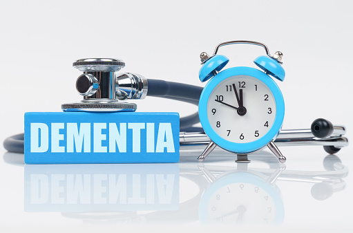 Medical concept. On a white surface there is an alarm clock, a stethoscope and a blue block with the inscription - DEMENTIA