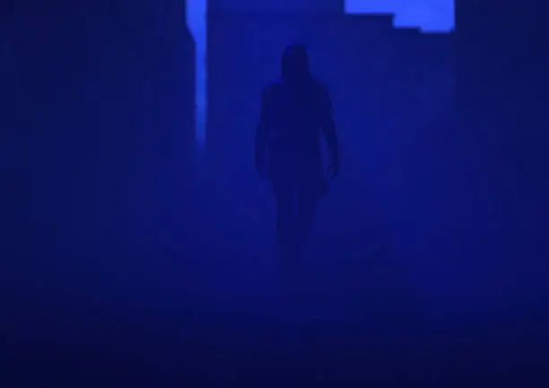 Mysterious man in a hoodie walks in a misty abandoned urban alley at dusk. 3D render.