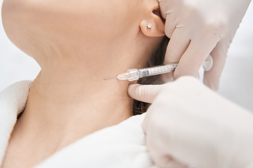 Close up of female client receiving rejuvenating neck injection in cosmetology clinic