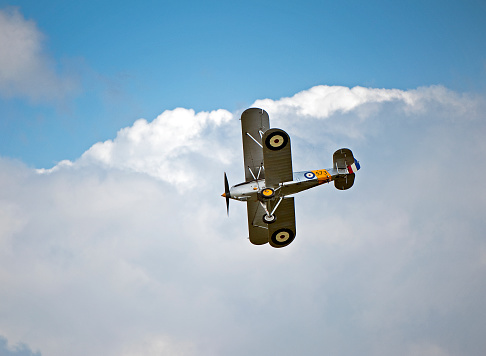 Hawker Nimrod Biplane in cloudscape setting, vicinity of Duxford, Camdridgeshire, England. Solo classic wartime single seat fighter aircraft flying in moody sky cloudscape over the fields of England