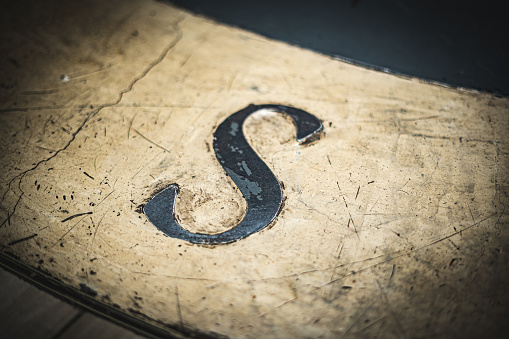 Letter S for south engraved in rusty metal on cement floor