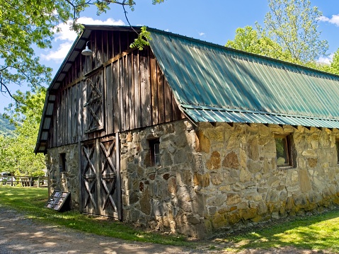Old stone barn with metal roof within the Todd and Ruth Henry park on the ground of the Maggie Valley United Methodist church, Maggie Valley North Carolina. On a sunny spring day, May 2022. Maintained old barn used for storage and hosting event at the church community grounds.