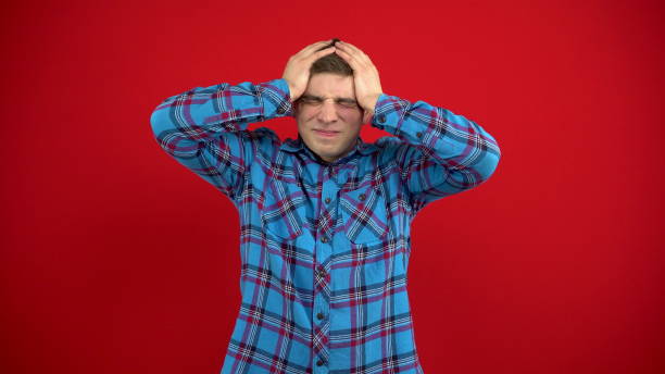 istock A young man has a headache and holds it in his hands. Shooting on a red background. 1397991982