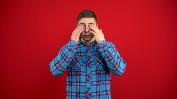 istock The young man's eyes hurt, he massages them with his hands. Shooting on a red background. 1397991995