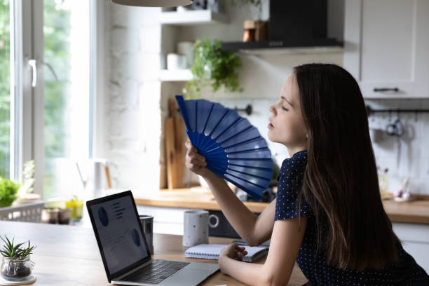 istock Young woman cools herself with handheld waver at home 1397993259