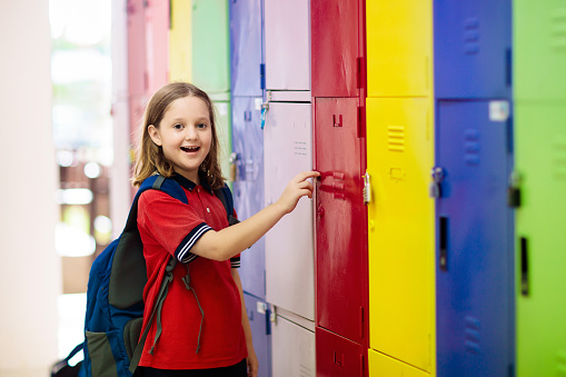 Portrait of elementary schoolgirl with classmates standing in front of lockers in school. Group of friends standing at their lockers together.