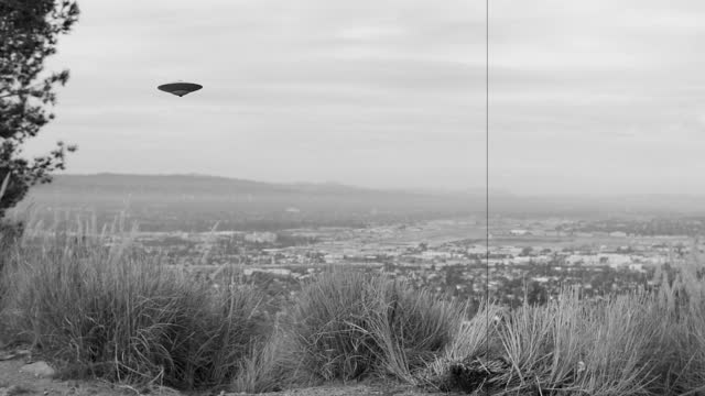 CLASSIC FLYING SAUCER HOVERS OVER AN URBAN VALLEY.