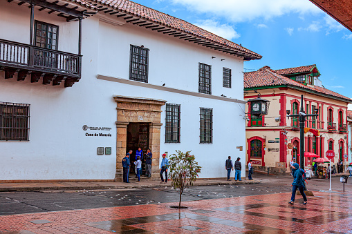 Bogotá, Colombia - July 20, 2016: A sudden thundershower has just ended on Calle or Street 11 in the historical La Candelaria district of Bogotá, the Andes capital city in the South American country of Colombia. The road and sidewalk are still wet. To the left of the image is the entrance to what was the old mint, and is today the Museum Casa de Moneda. The altitude at street level is about 8,660 feet above mean sea level. It is 20th July, National Day and a holiday in Colombia; the street is therefore not as busy as it would normally be. Photo shot on an overcast Afternoon; horizontal format.