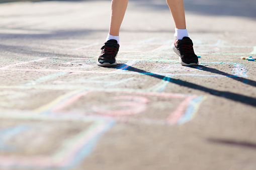 Kids play hopscotch in summer park. Healthy active outdoor game. Children playing and drawing with chalk on suburban city street. Boy and girl jump. Hop scotch fun for young child. Kid jumping.