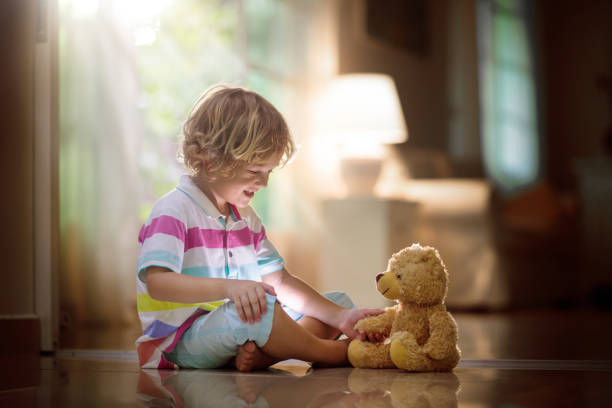 Child playing with teddy bear. Little boy hugging his favorite toy. Kid and stuffed animal at home. Toddler sitting on the floor of living room with big window at sun set. Kids play indoors.