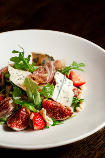 Salad with hamon ham, figs, blue cheese, arugula and strawberry on a plate. Dark Wooden background.