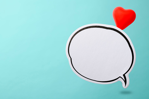 Red heart shape from blank speech bubble against light blue background with copy space.