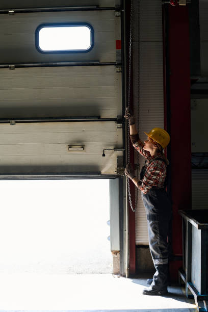 istock Young female engineer opening shutter roller door of garage, hangar or workshop 1398013383