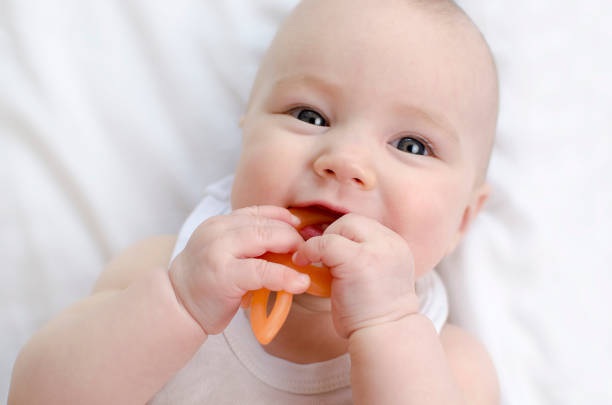 赤ちゃんは最初の歯を育てます。かわいい新生児、ベッドクローズアップで噛む歯。 - finger in mouth ストックフォトと画像
