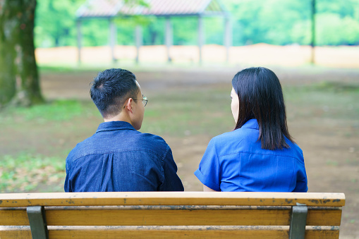 Back view of a young couple chatting on a bench in a green park
