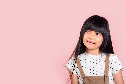 Asian little kid 10 years old looking away to side natural expression at studio shot isolated on pink background, Portrait of Happy child girl smiling staring away thinking
