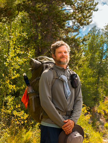 Portrait of smiling middle aged bearded male hiker in Rocky Mountains, Colorado; trees in background
