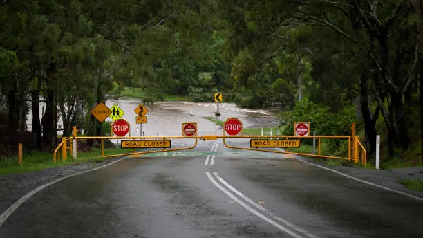Photo of Floodway. Bright Yellow and Red Stop signs warning motorists that the road is closed and flooded. Youngs Crossing, Petrie, Queensland, Australia.
