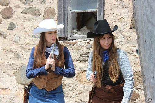 Cowgirls in a barn wearing denim, fringed clothing, a gun and boots, western clothing, guns drawn
