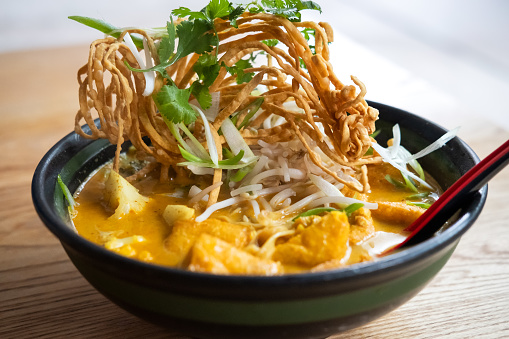 Vegan Khao Soi (Thai Coconut Curry Noodle Soup) with cauliflower, tofu puffs and garnished with bean sprouts, crispy fried noodles, cilantro and green onions.