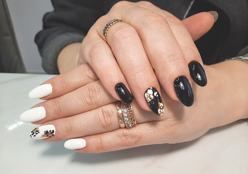 Women's hands with a beautiful black and white gel polish. Black and white manicure with abstract gold design spots.