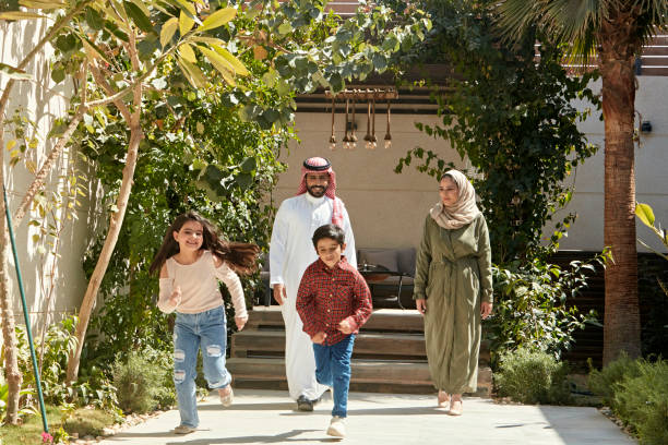 Active Saudi children outdoors with their parents Full length front view of 6 and 7 year old siblings in casual clothing leaving shaded patio and running towards camera with smiling parents following behind. saudi arabia stock pictures, royalty-free photos & images