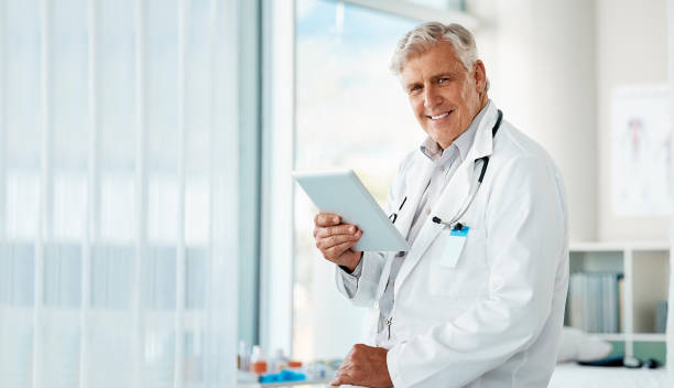 istock Happy mature male doctor holding a digital tablet. Smiling senior practitioner using digital tablet to check medical records or results in a hospital 1398050744