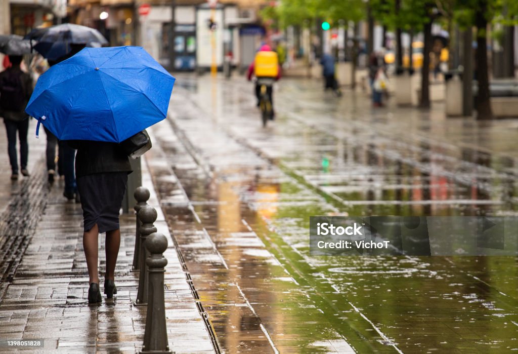 City life in a rainy day Unrecognizable woman with blue umbrella walking down city street in a rainy weather Rain Stock Photo