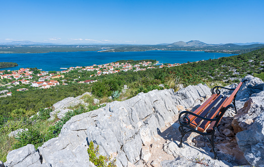 A bench on a hill overlooking  a coastal village. Down below is a lake connected to Adriatic sea, and thus combining fresh and salty water.