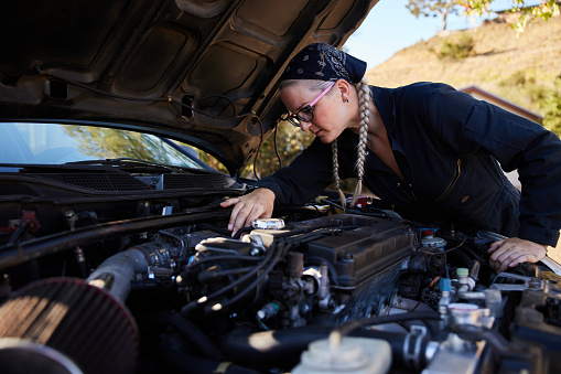 Young female mechanic inspecting the engine block of a car while doing some repairs outside of her workshop