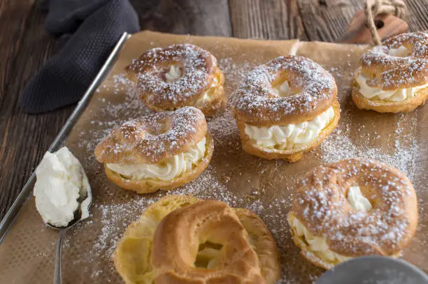 Delicious fresh baked cream puffs or profiterole filled with whipped cream and served on a baking tray on rustic and wooden table background.