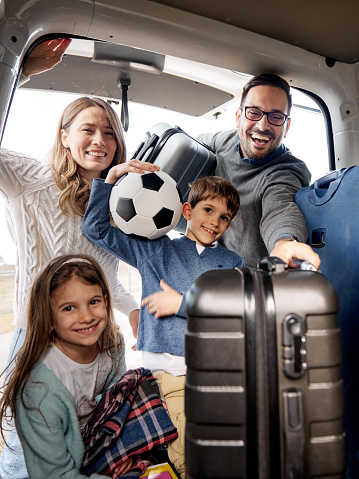 Happy parents and their kids cooperating while unloading their luggage after a trip by car.