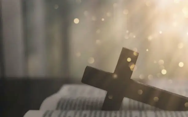 A cross and a Bible on a wooden table with bokeh lights from above. Concept, faith, hope, trust in God.