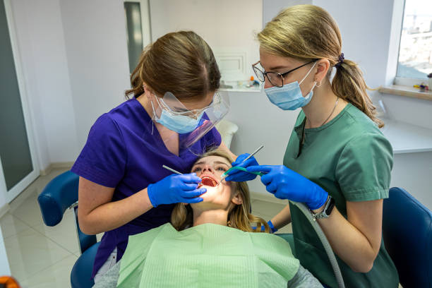 симпатичная пациентка сидит в кресле, в то время как врач с ассистентом осматривает ее зубы - dental assistent стоковые фото и изображения