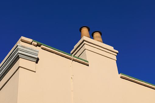 Close-up on a side wall of a building with chimney and deep blue sky beyond.