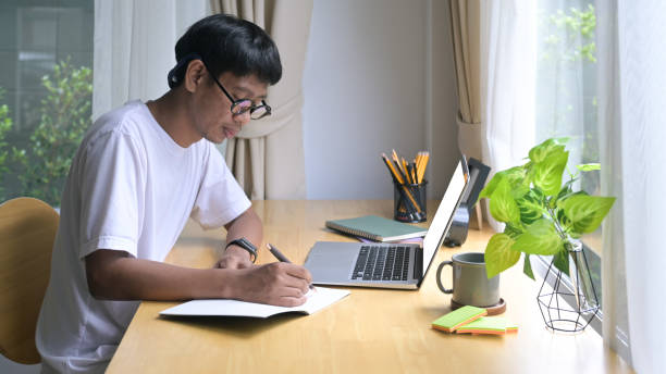 istock Side view young male freelancer using laptop, working online at home. 1398063621