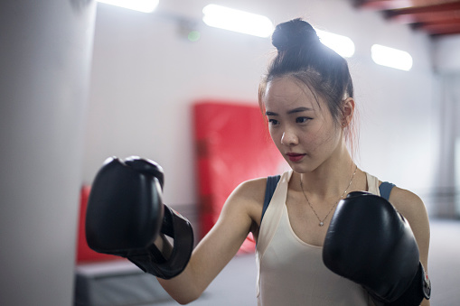 Asian Chinese Girl working out with boxing gloves and punching bag