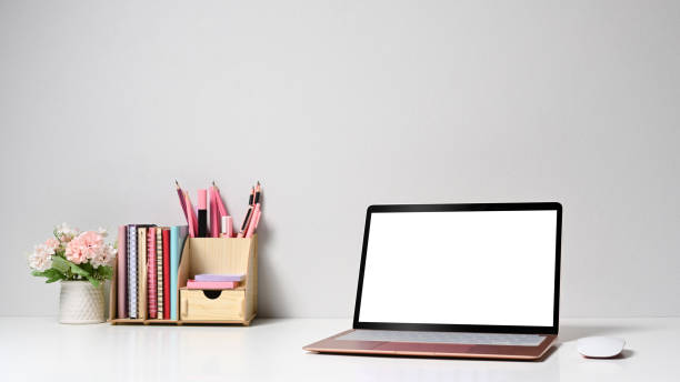 istock Front view computer laptop, flower pot and stationery on white table. 1398063766