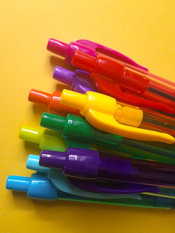 Vertical photo on yellow neon background
close-up of grouping of 10 brightly colored, sparkling retractable pens. Aligned on the right.
The reading from bottom to top of colors: turquoise, blue, purple, light green, green, yellow, orange, light purple, pink, red.