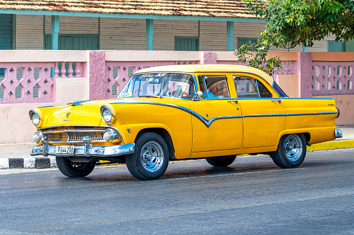 Varadero, Cuba - March 17, 2019: A man drives a yellow vintage car working as a private taxi in the First Avenue. Old vehicles are a profitable small business for its owners as they are popular with tourists.