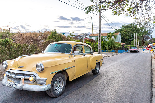 Varadero, Cuba - March 17, 2019: A cream colored vintage Chevrolet car drives away from the Todo en Uno commercial center. These old vehicles are tourist attractions.
