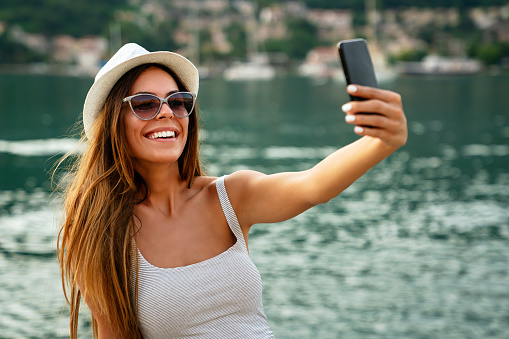 Beautiful woman having a good time at the beach on summer vacation, taking a selfie. People technology social media concept.