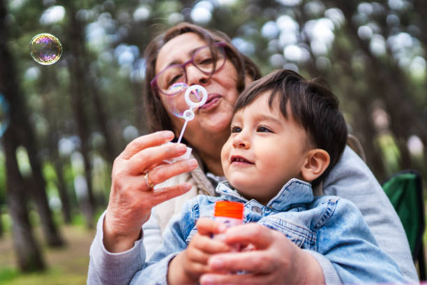 garotinho e sua avó brincando juntos em piquenique - bubble wand bubble child playful - fotografias e filmes do acervo