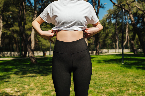 Young sportive woman wearing black yoga pant and white tees standing on a park bench.