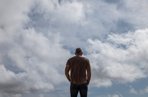 Rear view of adult man against cloudy sky