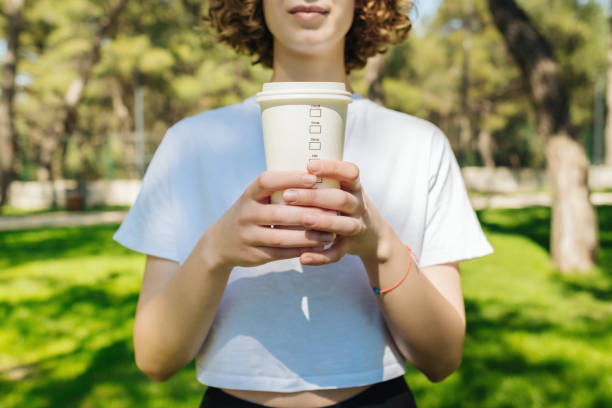 Young red head woman wearing white tee holding a paper cup of coffee takeaway front of her chest. Praying, relaxing, breathing concepts. stock photo