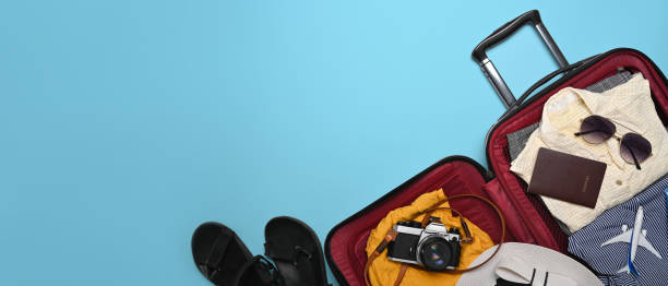 istock Open suitcase with camera, sunglasses, passport and clothes on blue background. Preparing for the summer vacations. 1398069259
